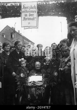 'Alsatians et Lorraine résident de retour dans la région occupée par les Allemands.Sur la photo : un groupe de personnes entoure une vieille femme en fauteuil roulant dans sa ville natale.Ils sont debout devant une arcade sur laquelle une affiche lit ''Bienvenue à la maison![traduction automatique]' Banque D'Images