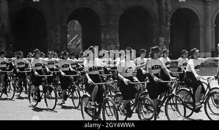 Une cohorte de femmes cyclistes passent devant le Colisée de Rome lors d'un défilé en 1939.Les cyclistes se tiennent chacun sur l'épaule droite du prochain pilote avec leur main gauche, formant des rangées.Les filles de Turin appartiennent à la Gioventu Italiana del Littorio, l'organisation fasciste de jeunesse italienne.[traduction automatique] Banque D'Images