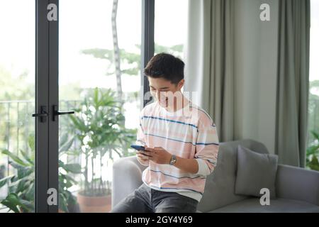 Jeune homme assis détendu sur canapé avec son ordinateur portable smartphone contrôle messages Banque D'Images