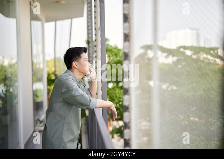 Vue en contre-plongée d'un jeune homme souriant parlant sur un téléphone portable, debout sur une terrasse de balcon Banque D'Images