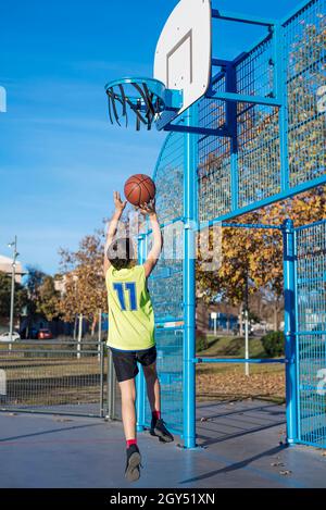 Un adolescent qui jette un ballon de basket-ball dans le panier par derrière Banque D'Images