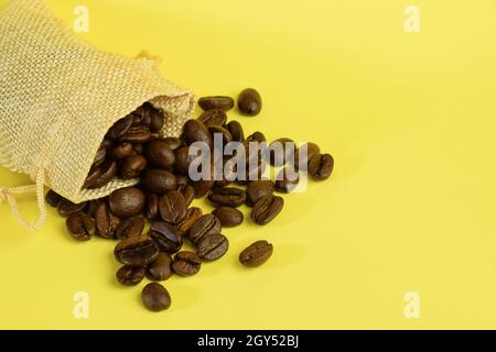 Grains de café dispersés dans un petit sac sur un fond jaune sur le côté gauche.Gros plan photographié.Côté droit pour l'étiquetage, vierge Banque D'Images