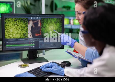 Équipe pluriethnique de chimistes chercheurs analysant des plantes génétiquement modifiées expertise sur le travail informatique en laboratoire hospitalier, divers biologistes examinant le test ogm en laboratoire Banque D'Images
