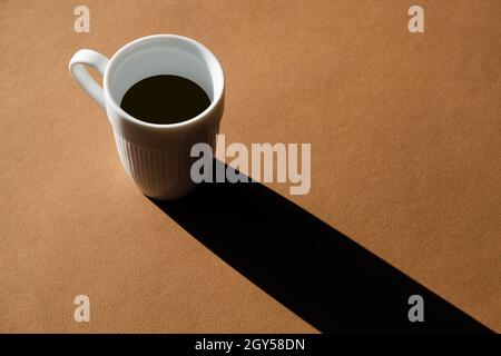 Une tasse de café sur fond marron projette une ombre longue. Banque D'Images