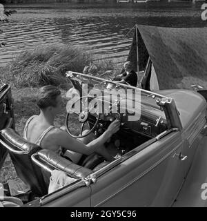 Ein Mann am Steuer eines Ford V8 Cabrio vor einem Klepper Zelt am einem Voir, Deutschland 1930 er Jahre. Un homme au volant de sa Ford V8 convertible en face d'un Klepper tente sur la rive d'un lac, l'Allemagne des années 1930. Banque D'Images