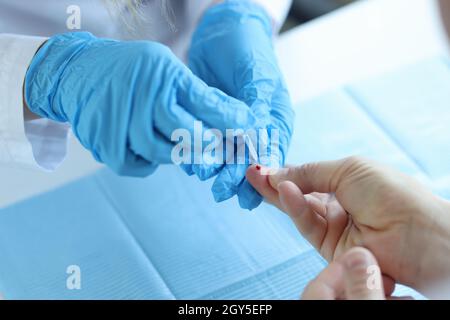 Le médecin portant des gants jetables prend le sang du doigt du patient Banque D'Images