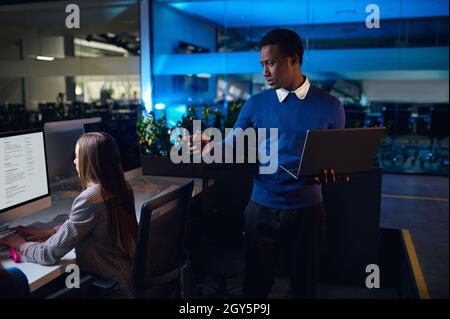Deux directeurs travaillent dans le bureau de nuit.Hommes et femmes souriants, centre d'affaires sombre à l'intérieur sur fond, lieu de travail moderne Banque D'Images