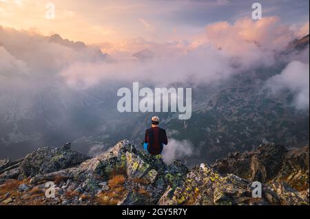 Un randonneur prend une pause et bénéficie d'une vue sur la montagne.Randonneur mâle assis sur le bord du pic et appréciant la vue sur la vallée des montagnes pendant le mal lourd Banque D'Images