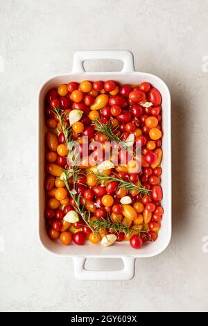 Vue panoramique sur un plat blanc rempli de tomates cerises, d'ail, de romarin, d'huile d'olive et de flocons de sel de mer Banque D'Images