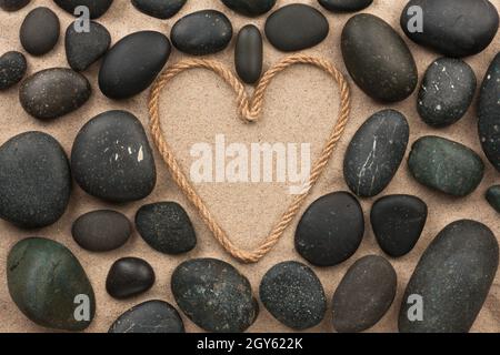 Beau cadre de corde dans la forme de coeur avec les pierres noires, sur le sable Banque D'Images