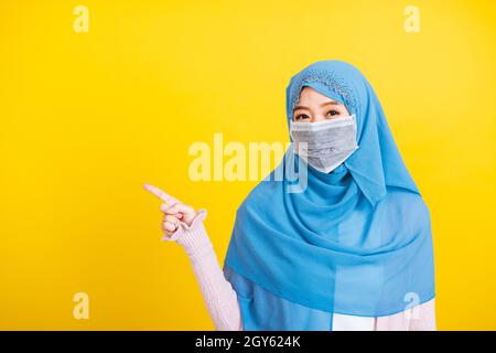Arabe musulman asiatique, Portrait de la jeune femme heureuse belle religieuse porter voile hijab et masque protecteur pour empêcher le coronavirus qu'elle pointe pointer de courbare Banque D'Images