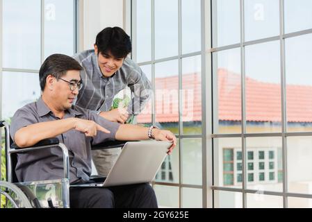 Homme d'affaires asiatique senior handicapé en fauteuil roulant avec ordinateur portable discuter avec l'équipe au bureau. L'homme du vieux père assis en fauteuil roulant et son Banque D'Images