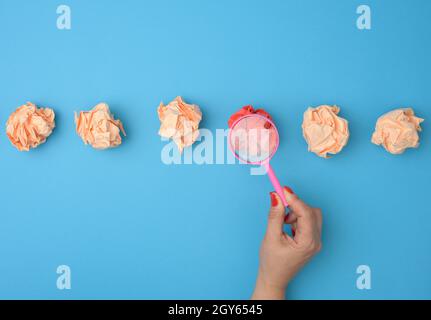 la main femelle tient une loupe sur des boules de papier froissés. Concept de recherche et de sélection d'idées, brainstorming, résolution de problèmes en busine Banque D'Images