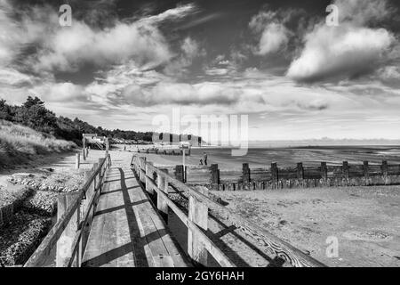 Promenade menant à des cabanes de plage et de plage donnant sur la baie de Holkham à Well-Next-the-Sea sur un matin lumineux et ensoleillé d'octobre en Monochrome Banque D'Images