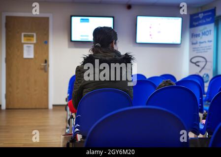 Une patiente de race mixte assise dans la salle d'attente d'une chirurgie GP pendant une pandémie Banque D'Images
