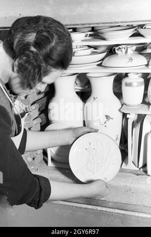 Eine der Staatlichen Porzellanmanufaktur Keramikerin Berlin stellt einen bemalten Teller dans den Brennofen Glattbrand für den 1930er Jahre, Deutschland. Un céramiste de la Manufacture de Porcelaine d'État Berlin met une plaque peinte à l'intérieur du four pour la cuisson, glost Allemagne 1930. Banque D'Images