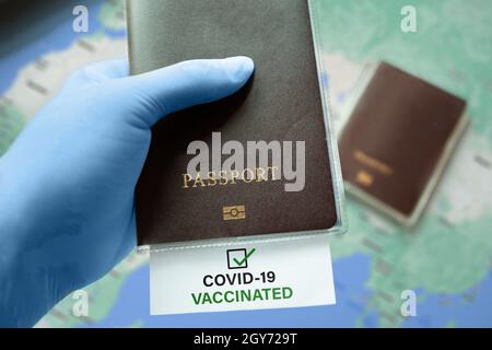 Mains dans des gants médicaux portant un passeport avec une note vaccinée COVID-19 avec une coche sur la carte. Situation d'éclosion de coronavirus, en voyage après une pandémie Banque D'Images