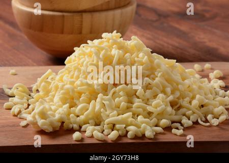 Tas de fromage râpé sur petit panneau en bois. Fromage râpé pour la cuisson sur une planche à découper sur fond de bois Banque D'Images