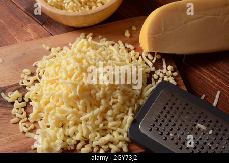 Tas de fromage râpé sur petit panneau en bois. Fromage râpé pour la cuisson sur une planche à découper sur fond de bois Banque D'Images