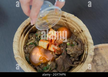 Femme main avec le gyudon japonais avec oeuf ou bol de boeuf japonais avec oeuf dans bol de feuille de banan biologique Banque D'Images