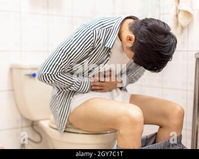 Le jeune homme tenant son abdomen se sent malade et la constipation dans les toilettes Banque D'Images