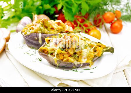 Aubergine farcie au fromage fumé, tomates, oignons, carottes à l'ail, fromage et herbes dans une assiette sur une serviette de cuisine sur fond de woo léger Banque D'Images