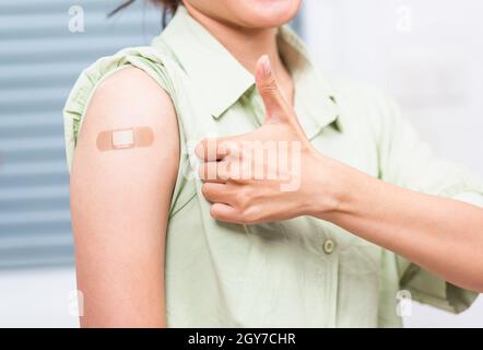 Jeune femme asiatique montrant le pouce gestante vers le haut ou comme et son bras avec bande de plâtre aide après le coronavirus Covid-19 injection sur l'épaule, coron Banque D'Images