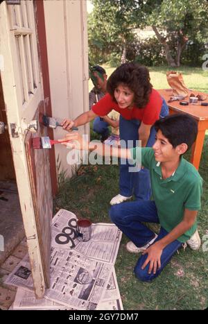 Austin Texas USA, 1988: La mère hispanique et son fils aide à l'entretien de la maison en peignant la porte du hangar de cour arrière.©Bob Daemmrich Banque D'Images