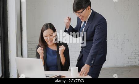 Oui ! Heureux excité réussi, homme d'affaires asiatique et femme sourire station de travail triomphant avec les mains levées avec ordinateur portable, femme succès Banque D'Images