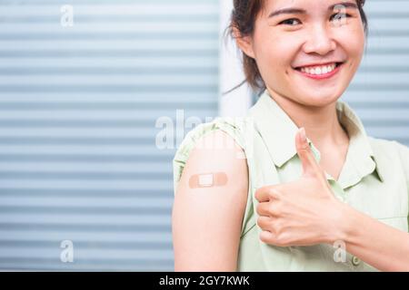 Jeune femme asiatique montrant le pouce gestante vers le haut ou comme et son bras avec bande de plâtre aide après le coronavirus Covid-19 injection sur l'épaule, coron Banque D'Images