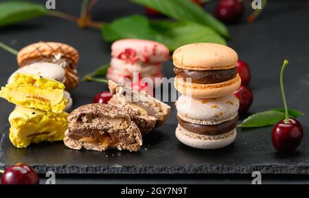 pile de macarons multicolores et de cerises rouges mûres sur fond de bois noir, gros plan Banque D'Images