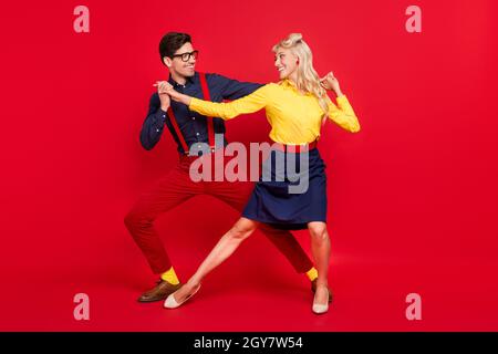 Vue sur toute la longueur de la taille du corps d'un couple attrayant et joyeux dansant de la torsion festive jour isolé sur fond rouge vif de couleur Banque D'Images
