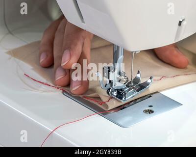 La couturière de la chambre est un couturier qui a réalisé un motif de fil de soie rouge sur un tissu beige fin. Gros plan Banque D'Images