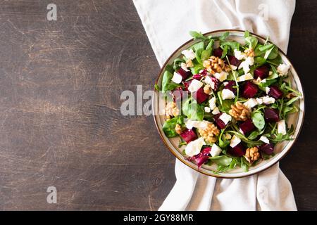 Salade de betteraves ou de betteraves avec roquette fraîche, fromage doux et noix sur l'assiette, vinaigrette et épices sur fond de bois foncé, espace pour les copies, vue du dessus/ Banque D'Images