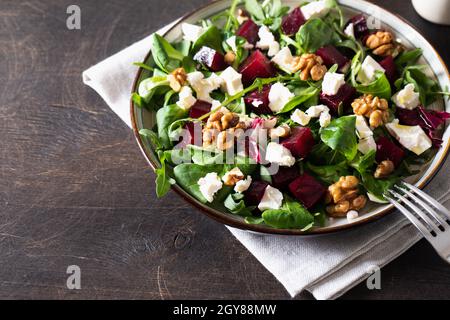 Salade de betteraves ou de betteraves avec roquette fraîche, fromage doux et noix sur l'assiette, vinaigrette et épices sur fond de bois foncé, espace pour les copies, vue du dessus/ Banque D'Images