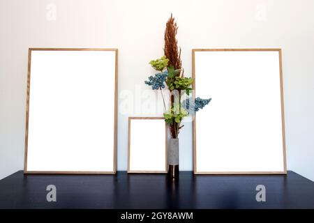 Trois cadres en toile, photo ou photo pour l'espace de copie près du mur blanc sur table en bois avec usine de maison décorative, intérieur élégant espace de décoration pour Banque D'Images