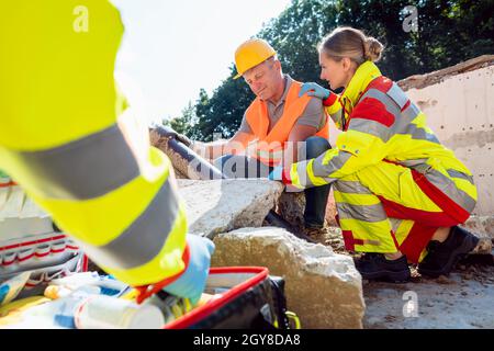 Les médecins d'urgence qui donnent des premiers soins au travailleur de la construction qui parle à l'homme Banque D'Images