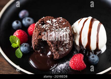 Gâteau fondant au chocolat avec baies et glace à la vanille sur une assiette noire, vue rapprochée.Dessert sucré Banque D'Images