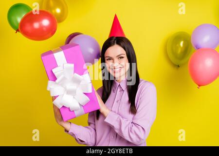 Photo de funky brun coiffure millénaire dame tenir présent ballons mouche porter chapeau anniversaire chemise rose isolée sur fond jaune Banque D'Images