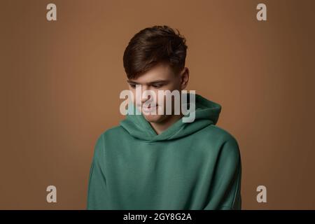 un jeune garçon contrarié dans un sweat-shirt isolé sur fond marron. Émotions humaines, expressions du visage Banque D'Images