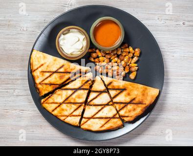 Vue de dessus de la Quesadilla coupée de tortilla pliée remplie de fromage, viandes, épices avec sauces et graines de maïs frites sur plaque sur bois gris Banque D'Images