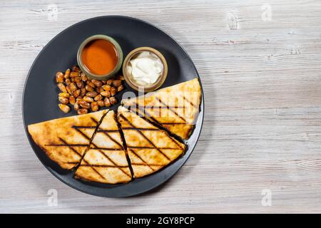 Vue de dessus de la Quesadilla coupée de tortilla pliée remplie de fromage, viandes, épices avec sauces et graines de maïs frites sur plaque en bois avec copys Banque D'Images