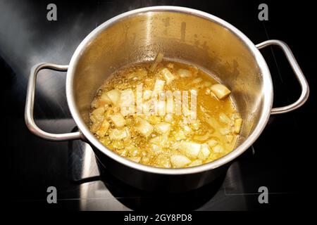 Les oignons sont sautés dans du beurre brun doré dans une casserole en acier inoxydable sur un poêle à induction noir, base de recettes de sauce ou de soupe, concept de cuisson, sélecte Banque D'Images