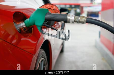 Buse de pompe à gaz benzène verte pour remplir le réservoir de voiture sport rouge. Gros plan Banque D'Images