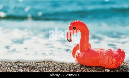 Flamants roses gonflables sur la plage avec mousse blanche de vague de mer. Été, vacances, natation, concept de station balnéaire avec flamants roses. Bannière. Copier la flèche Banque D'Images