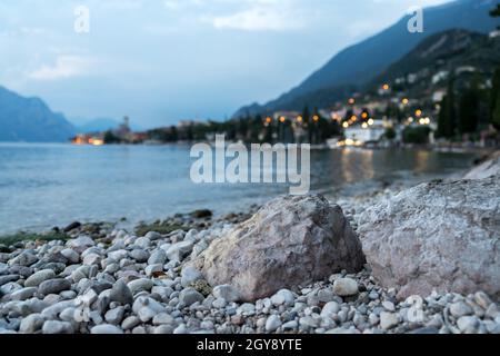 Rock à l'avant-plan, mignon petit village italien avec des lumières à l'arrière-plan. En soirée. Banque D'Images