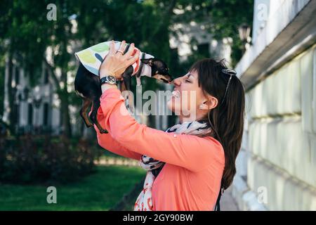 Bonne jeune femme caucasienne tenant son petit chien qui embrasse son visage.Russe Toy ou russe Toy Terrier, vêtu d'un costume d'automne.Animaux de compagnie adorés Banque D'Images