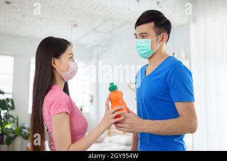 Jeune couple porter avec l'entraînement de masque médical ensemble et tenant la bouteille d'eau. Banque D'Images