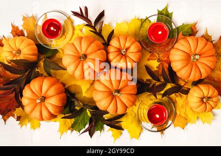 Feuilles d'érable multicolores, citrouilles et bougies sur fond de nappe blanche.Composition d'automne avec pose plate.Automne, automne, halloween, Thanksgiving Day concept. Banque D'Images