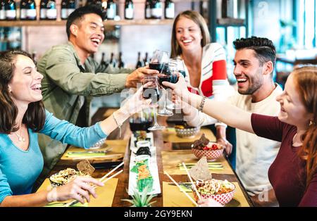 Des amis multiraciaux dégustent du vin rouge au restaurant sushi - concept de mode de vie de la nourriture et des boissons avec des gens heureux s'amuser ensemble au bar fusion Banque D'Images